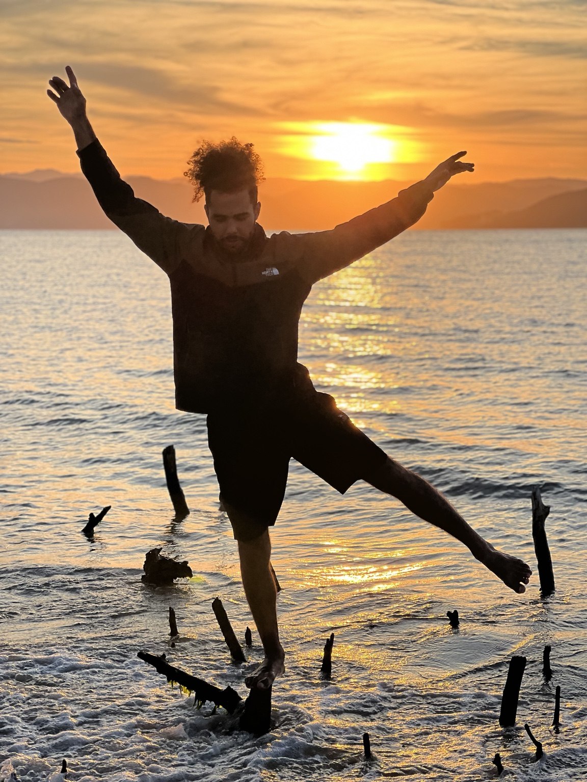 Gustavo praticando equilíbrio em uma linha junto à água ao pôr do sol