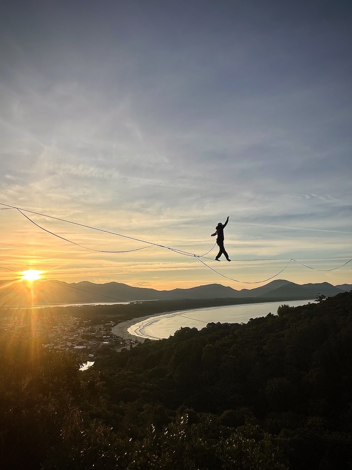 Atleta atravessando um highline sobre a paisagem ao pôr do sol